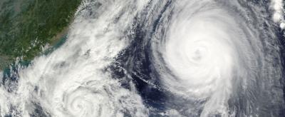 Satellite image of two large cyclones in the ocean near a landmass, with swirling cloud patterns visible.