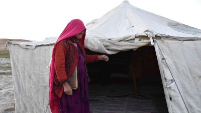 A person wearing a pink headscarf and red sweater stands outside a white tent.