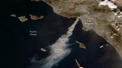 Satellite image showing smoke from wildfires near Los Angeles drifting over the Pacific Ocean. Land features and labels for Los Angeles and Pacific Ocean are visible.