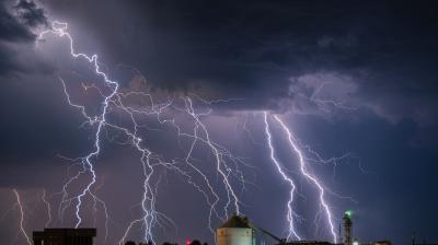 Multiple lightning bolts strike the ground near industrial buildings under a dark, cloudy night sky.