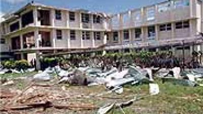 A two-story building with significant exterior damage, debris, and scattered materials covering the surrounding ground.