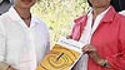 Two people standing outdoors holding a yellow book with a maze design on the cover, both facing the camera.