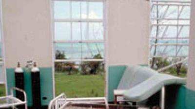 A hospital examination room with a hospital bed, oxygen tanks, and large windows overlooking a grassy area and a body of water.