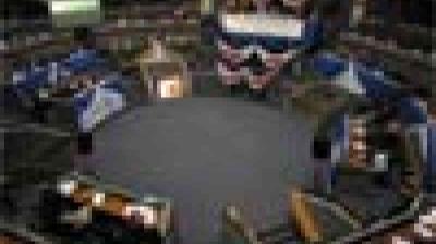 Blurry image of people seated in a circular arrangement around a central area, possibly in a meeting or conference setting.