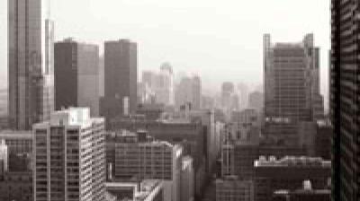 Black and white photo of a city skyline with tall buildings and skyscrapers under a hazy sky.