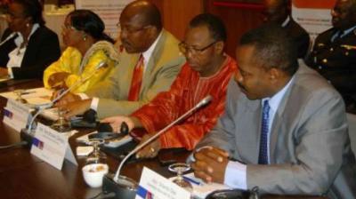 Four individuals sit at a conference table with microphones and documents, engaged in discussion at a formal meeting.
