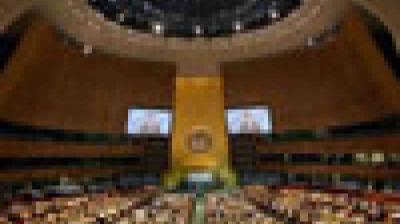 A large assembly hall filled with delegates seated in rows, featuring a central podium and the United Nations emblem on a golden wall.