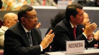 Two men in suits sit and applaud at a conference table with a sign labeled "Indonesia" in front of them.