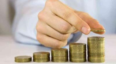 A person stacks coins in ascending order, showing an increasing progression of coin piles on a table.