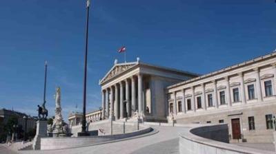 The image shows the Austrian Parliament building in Vienna, featuring neoclassical columns, statues, and the Austrian flag atop the main structure.