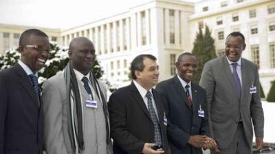 Five men in suits and conference badges stand outdoors in front of a large building, smiling and conversing on a winter day.