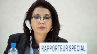 A woman wearing glasses and a headset sits at a desk with a sign reading "Rapporteur Special.