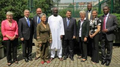 Ten people, dressed in business or formal attire, stand in a line outdoors on a stone path, posing for a group photo with trees and a building in the background.