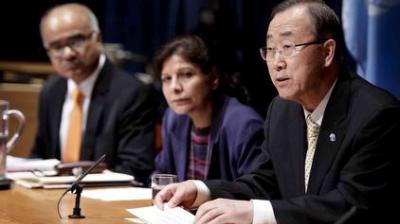 Three people sit at a table during a formal meeting; one man speaks into a microphone while the others listen attentively.
