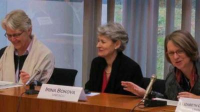 Three women sit at a conference table with microphones and nameplates, including one labeled "Irina Bokova UNESCO," participating in a formal discussion.