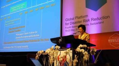 A woman speaks at a podium during the Global Platform for Disaster Risk Reduction conference in Geneva, with a presentation slide projected behind her.