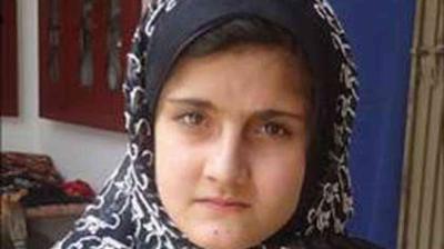 A young girl wearing a patterned black and white headscarf looks directly at the camera with a neutral expression.