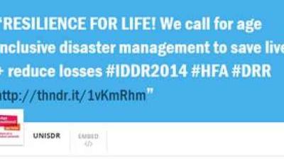 Blue banner with white text promoting age-inclusive disaster management, featuring hashtags #IDDR2014, #HFA, #DRR, and a shortened URL link.