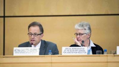 Two officials sit at a conference table with nameplates reading "Acting Director-General, United Nations Office at Geneva" and "Special Representative for Disaster Risk Reduction.