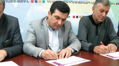 Three men seated at a table, two writing with pens on paper, against a backdrop with text and colored shapes.