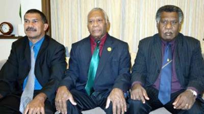Three men in suits sitting on a couch, facing the camera.