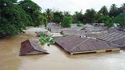 Flooded area with submerged houses and trees, showing rooftops barely above muddy water.