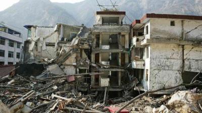 Collapsed buildings with debris scattered in front, set against a mountainous background.