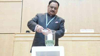A man in a suit places an object into a glass container filled with green items on a podium in a conference room.