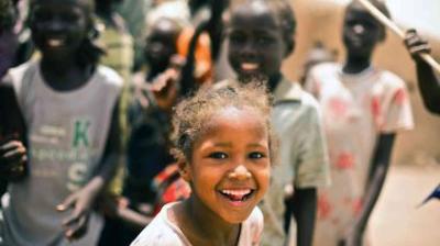 A group of children outdoors, with a smiling girl in the foreground.