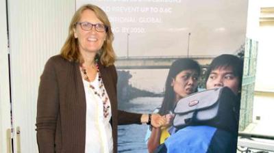 A woman stands next to a poster showing two people concernedly looking at something, with a bridge in the background.