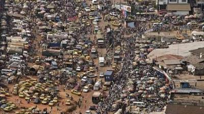 Aerial view of a crowded street filled with vehicles, market stalls, and a large number of people in an urban area.
