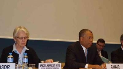 A meeting with a woman labeled "Special Representative" and a man labeled "Chair" seated at a table with nameplates and water bottles.