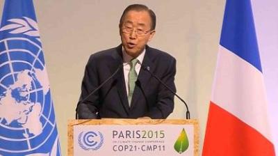 A man in a suit speaks at a podium labeled "Paris 2015 COP21-CMP11" with the UN and French flags in the background.