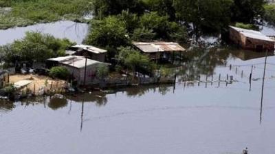 Aerial view of several small houses and trees partially submerged in floodwater, with fences and land barely visible above the waterline.