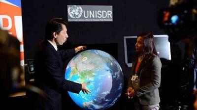 Two individuals are discussing a large digital globe display in front of a UNISDR sign.