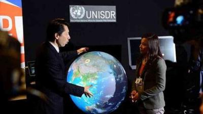 Two people converse in front of a digital globe display at a UNISDR (United Nations Office for Disaster Risk Reduction) event.