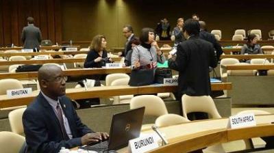 Delegates from various countries sit and converse in a conference room with country nameplates visible, including Burundi, South Africa, and Bhutan.