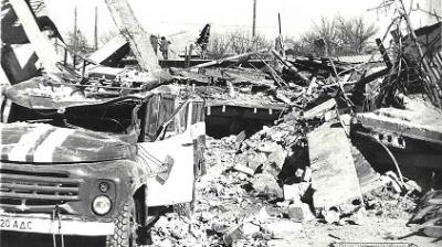 Black and white photo of a damaged truck amidst rubble and collapsed concrete structures, indicating a scene of destruction or aftermath.