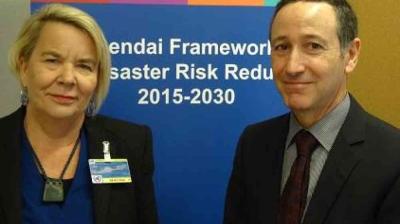 Two people stand in front of a sign that reads "Sendai Framework Disaster Risk Reduction 2015-2030.