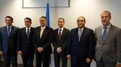 Six men in suits stand in a line in front of a flag.