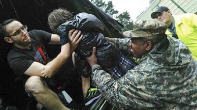 A man and a soldier help a child wearing a plastic cover climb into a vehicle as another person in a yellow raincoat watches.