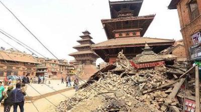A collapsed structure with debris in front of ancient temples, surrounded by a few people, and leaning power lines.