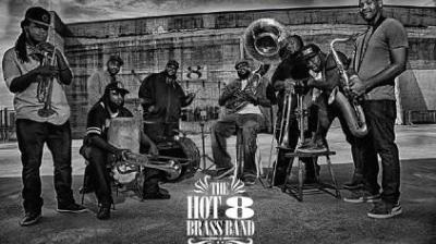 Black and white photo of a brass band with eight musicians holding instruments in an industrial setting.
