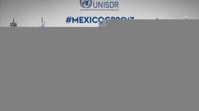 A conference panel for the UNISDR event #MEXICOGP2017, featuring speakers seated at a table with microphones and event branding in the background.