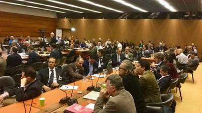A crowded conference room filled with seated attendees, discussing or listening to presentations.