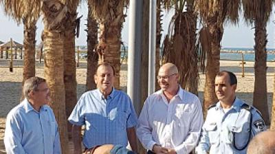 Four men stand together in front of palm trees on a sunny beach.