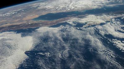 View of Earth from space showing a coastline with cloud formations and part of a continent visible under a layer of clouds.