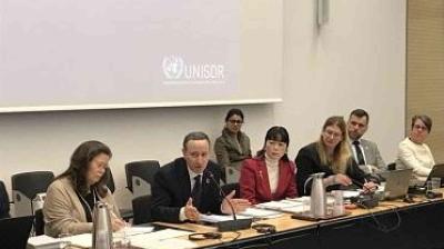 A panel of six people sits at a conference table with documents and microphones, with a UNISDR logo projected on the wall behind them.