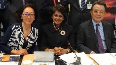 Three people are seated at a table with documents and microphones, posing for a group photo.