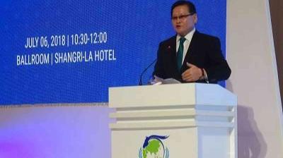 A man in a suit speaks at a podium during an event at Shangri-La Hotel, with a screen showing the date July 6, 2018, and event time 10:30-12:00.